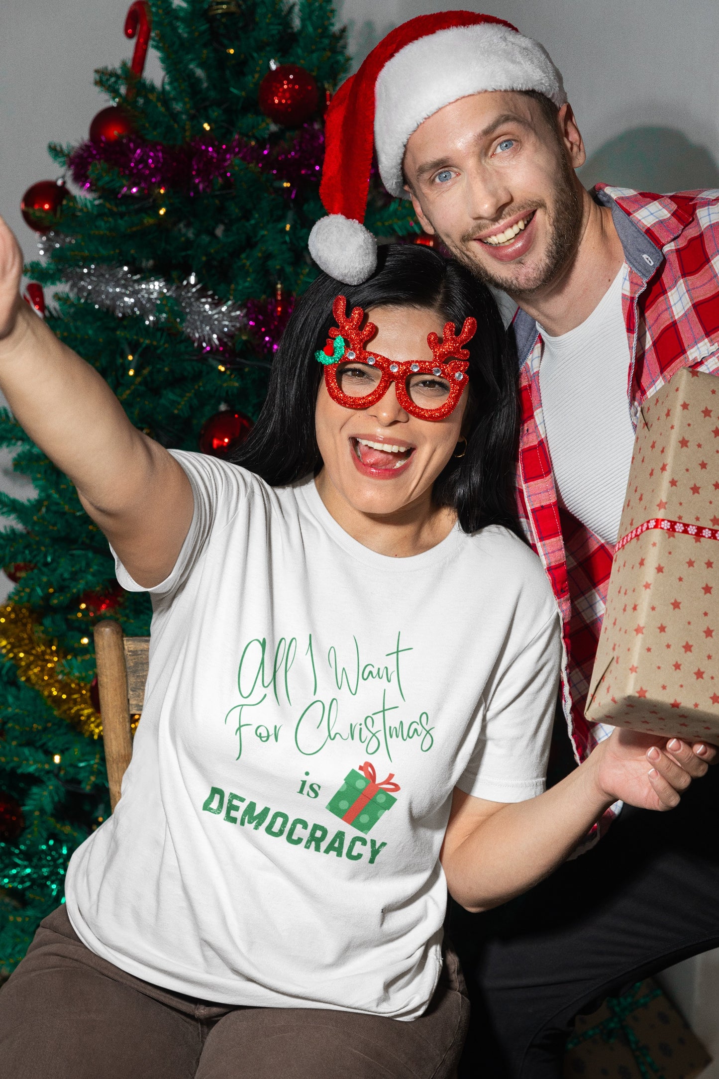 Two people celebrating Christmas with festive attire and a gift in front of a decorated tree.