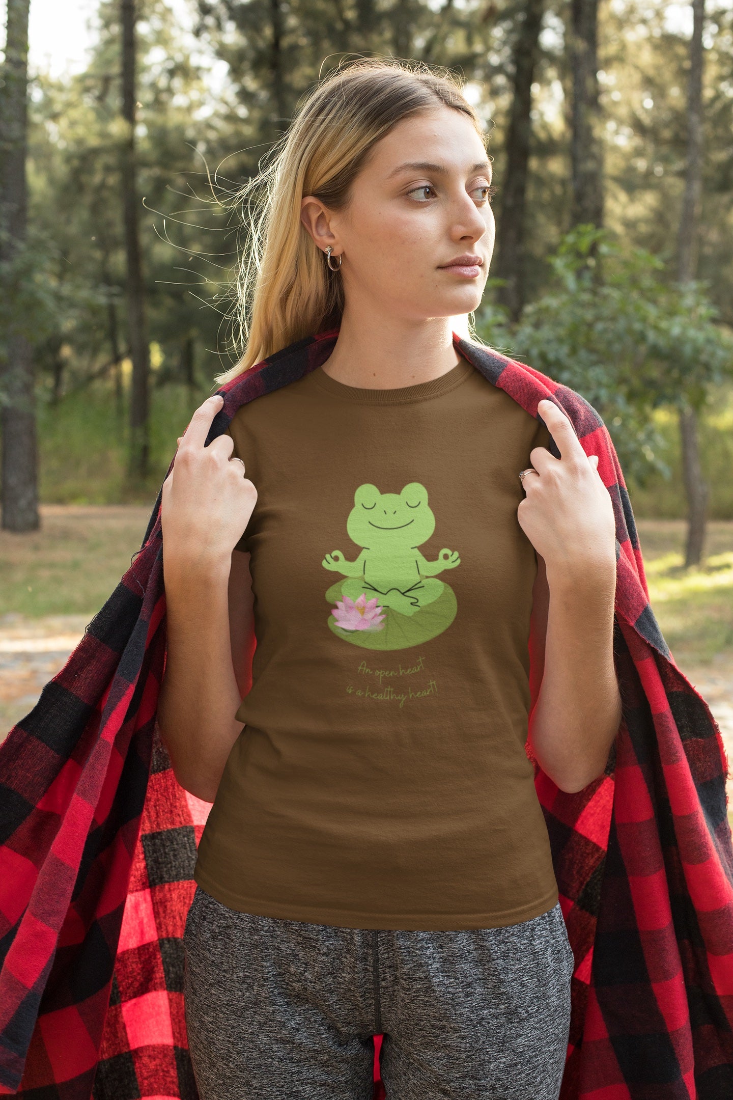 Woman wearing a brown t-shirt with a frog graphic in a forest setting
