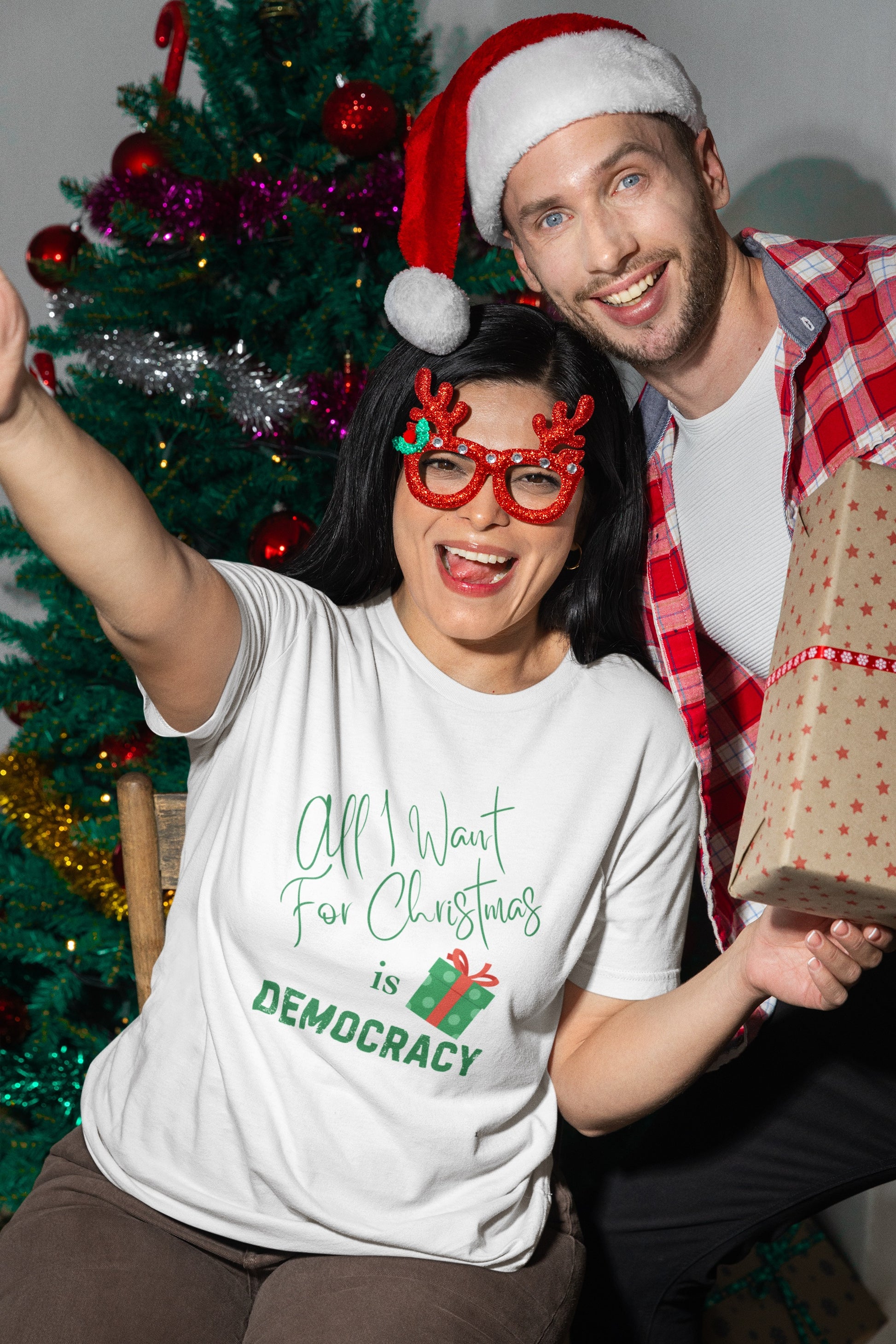 Two people celebrating Christmas with festive attire and a gift in front of a decorated tree.