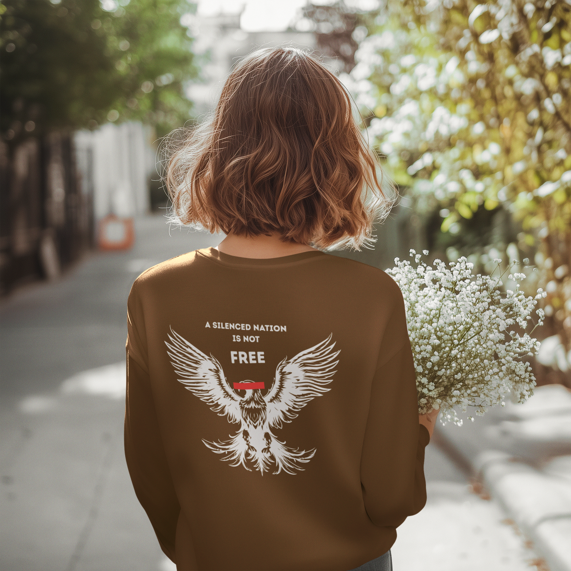 Person wearing a brown sweatshirt with an eagle design and text, standing outdoors.