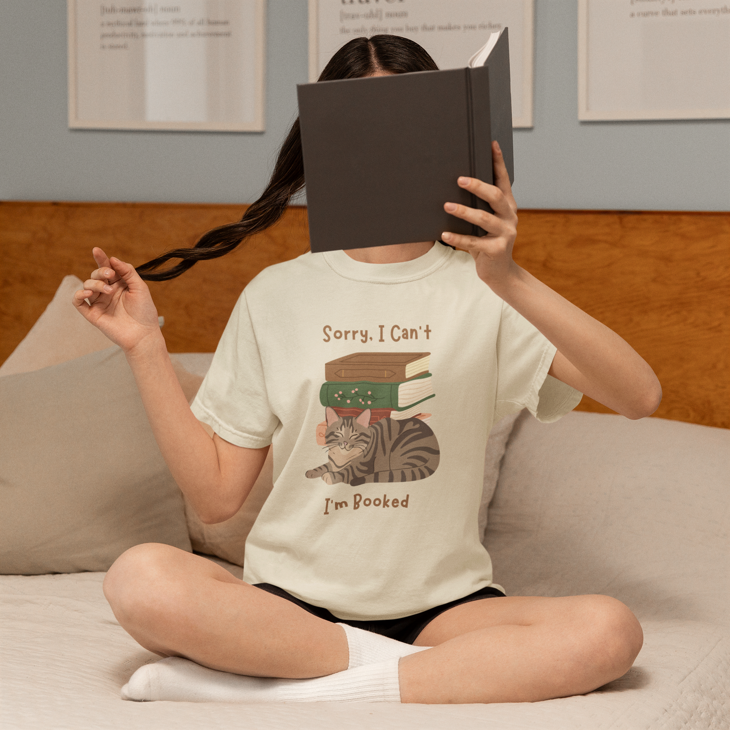 Ivory cotton tshirt with graphic of a cat laying in front of stack of books.  Text says, Sorry, I can't.  I'm booked.