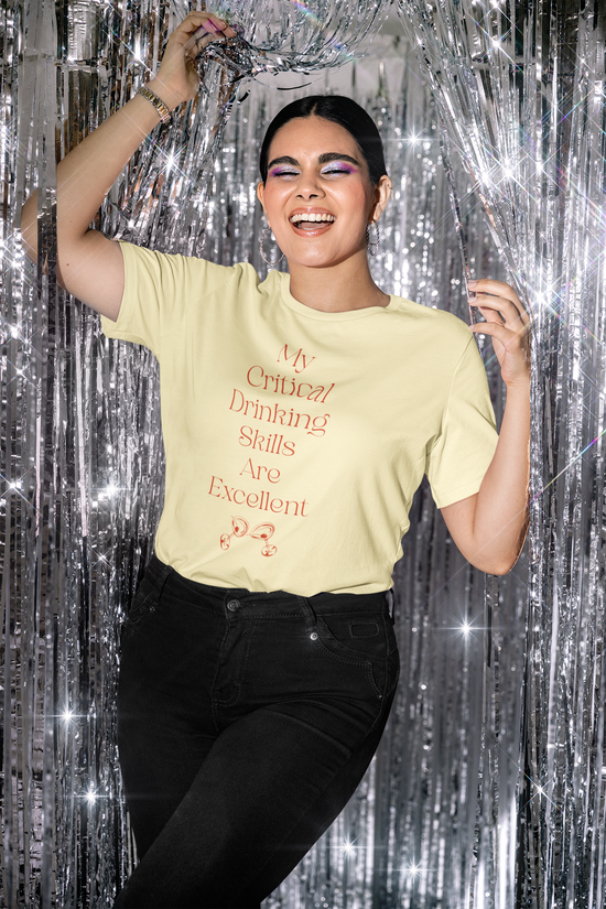 Yellow short sleeve, crew neck t-shirt has text that says "My critical drinking skills are excellent" and  a graphic of two martini glasses.  Worn by woman.
