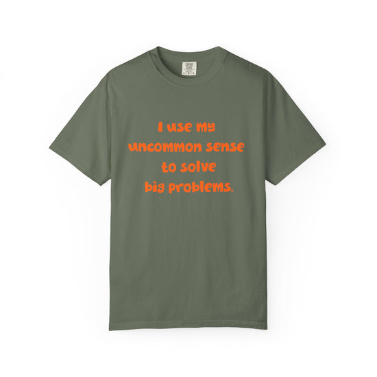 Green short sleeve, crew neck t-shirt has orange type that says "I use my uncommon sense to solve big problems."