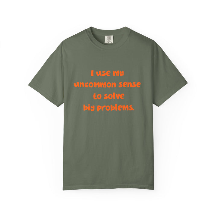 Green short sleeve, crew neck t-shirt has orange type that says "I use my uncommon sense to solve big problems."