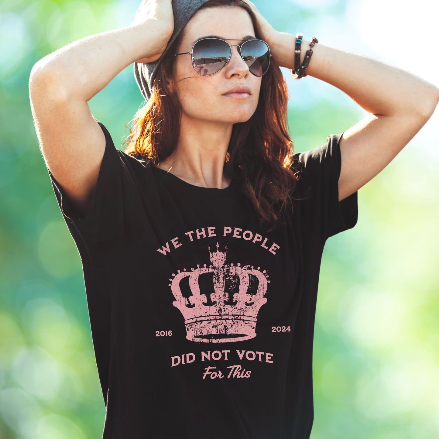 Blac t-shirt with pink text and crown graphic and text says 'No Kings' worn by woman