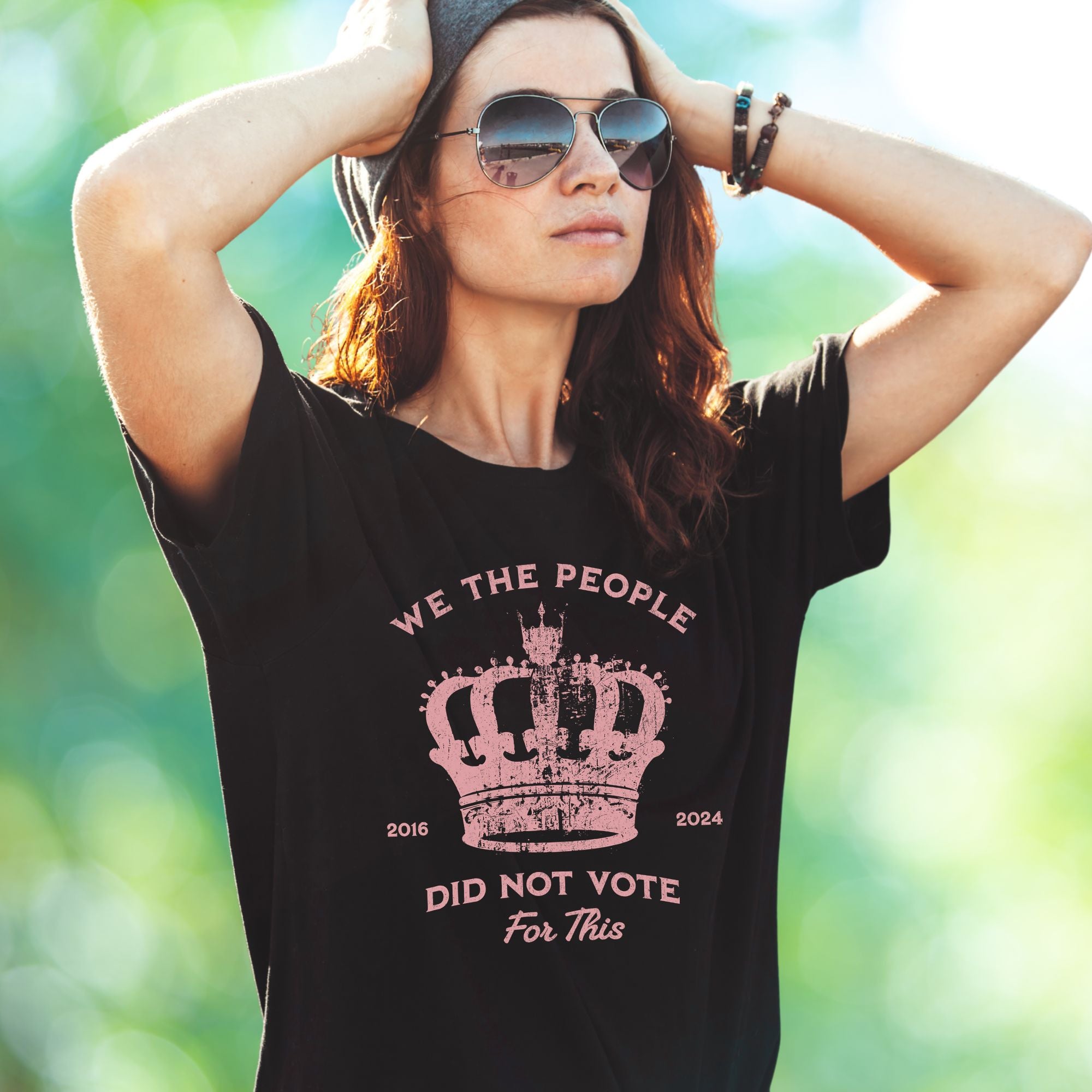 Blac t-shirt with pink text and crown graphic and text says 'No Kings' worn by woman