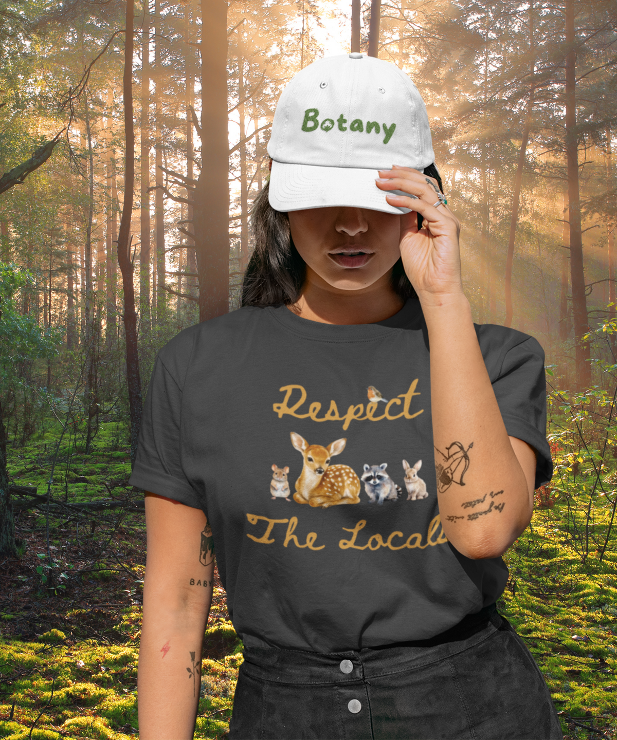 A vintage black short-sleeve crewneck t-shirt featuring a graphic print of a fawn, a raccoon, and a rabbit under the text 'Respect The Locals' in orange-brown script. Worn by woman in baseball cap