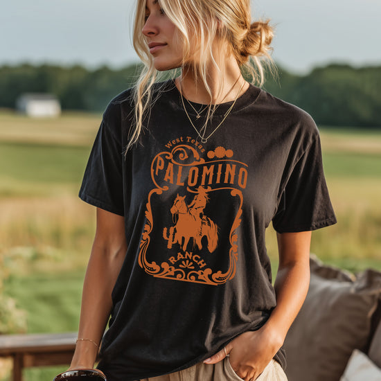 Black t-shirt with a graphic design of a horse and rider, and 'Palomino Ranch' text .Worn by woman